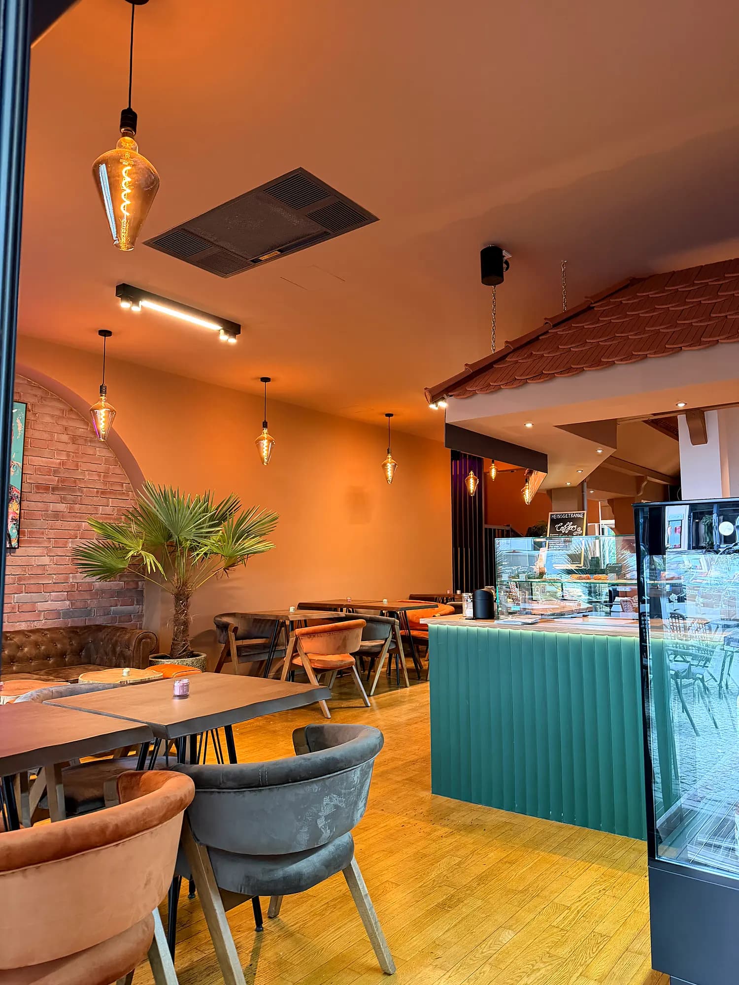 Dining room with a green counter and cake display, tables with upholstered chairs in front