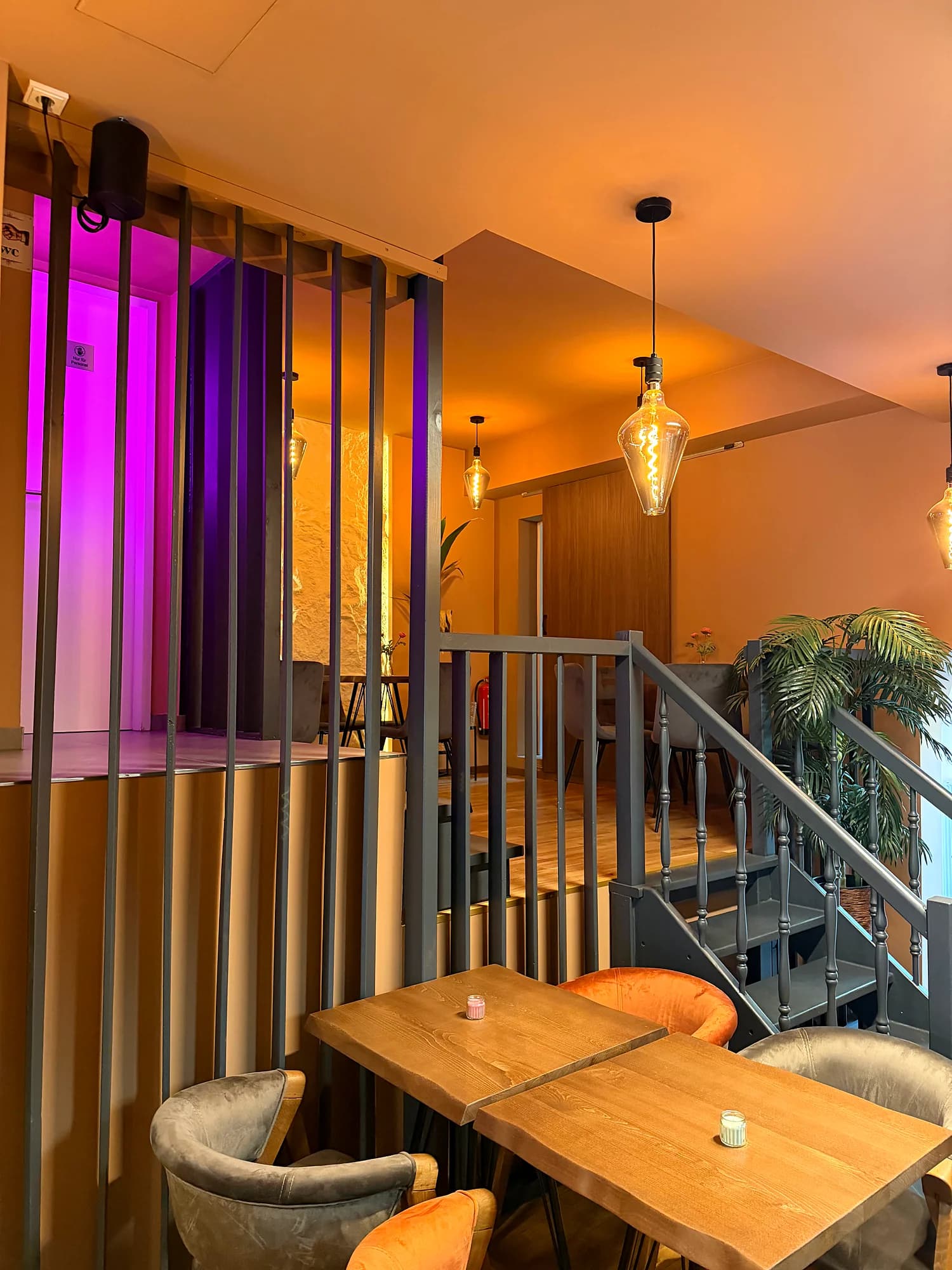 Metal stairs to the gallery with purple-lit wooden slats, two wooden tables in front