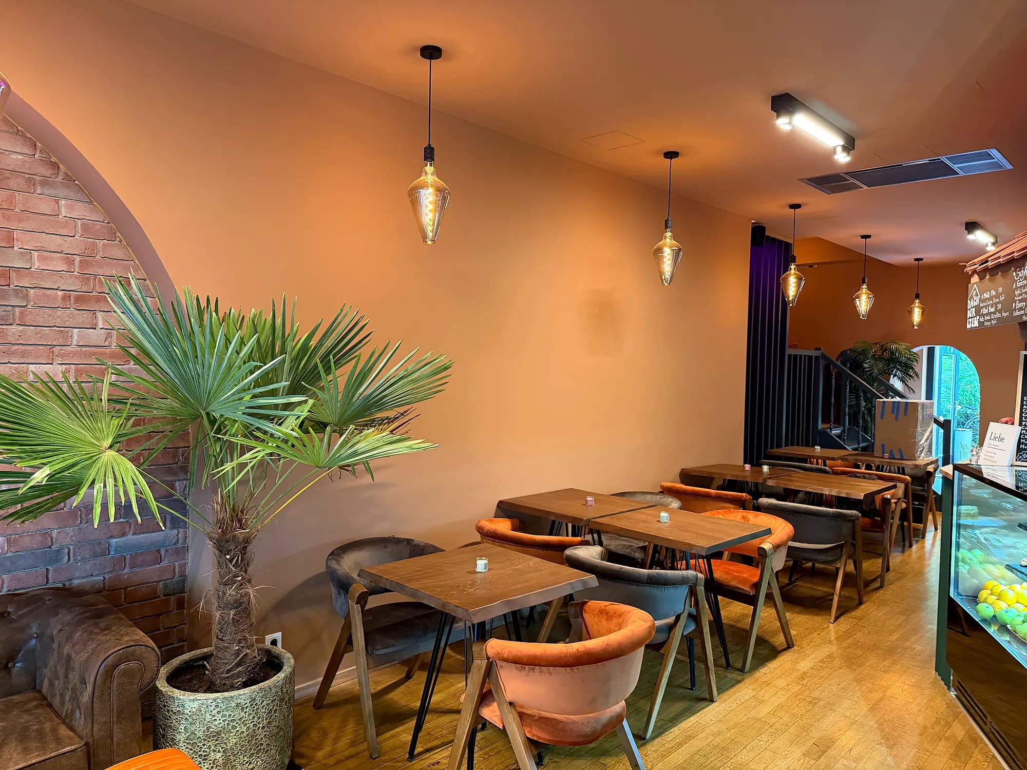 Dining room with a brick arch, a palm, wooden tables and upholstered chairs under pendant lamps