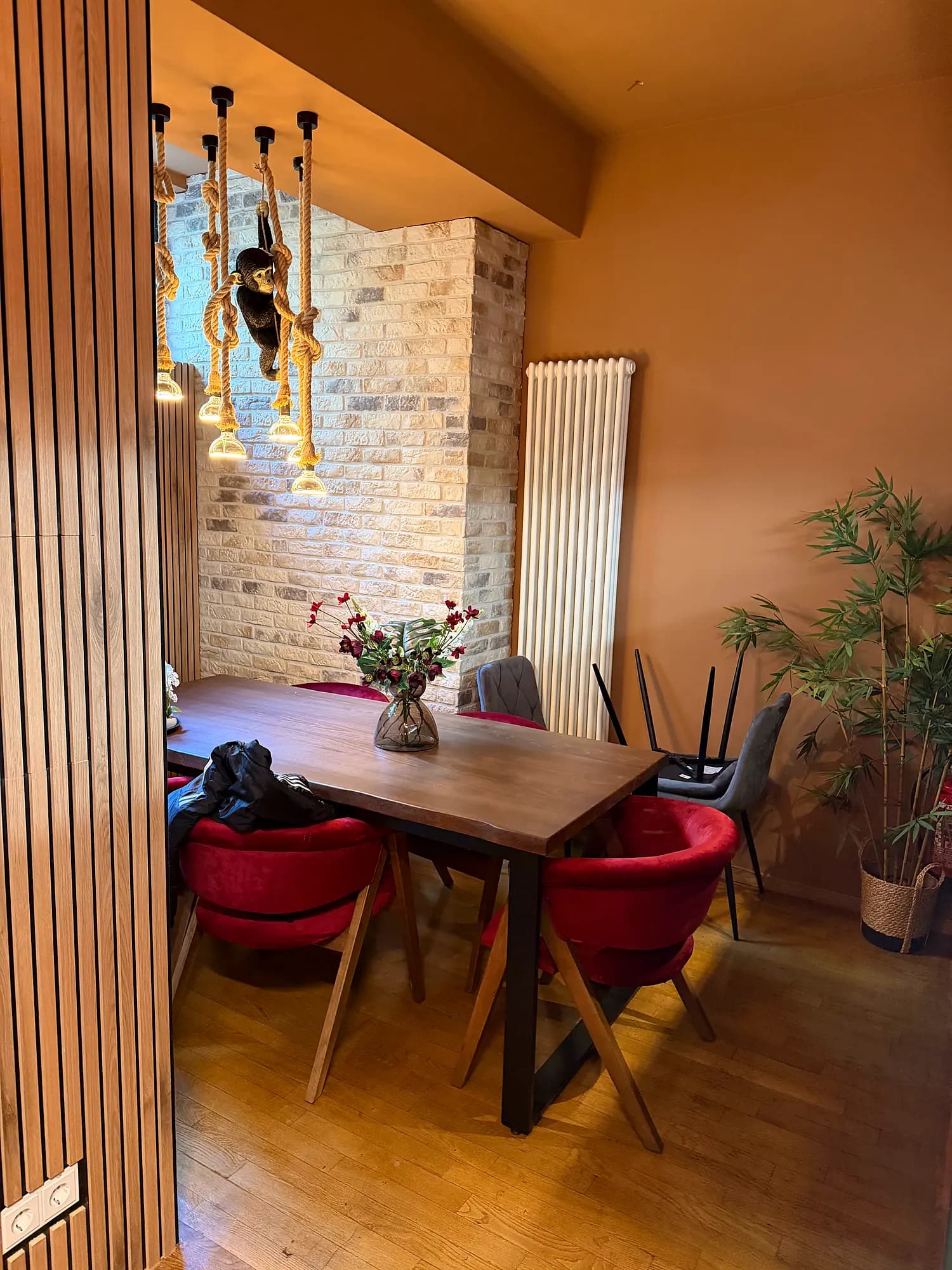 Private nook with a wooden table, red upholstered chairs, a brick wall and a monkey lamp on ropes